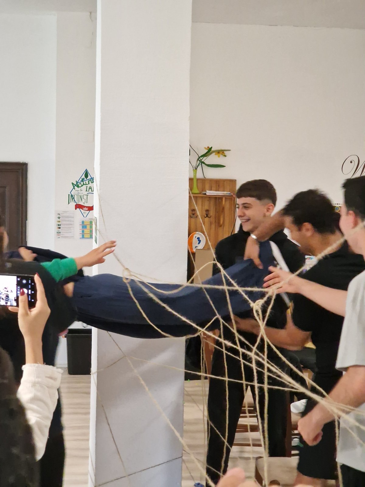 A participant is lifted horizontally and passed through the spider web of strings