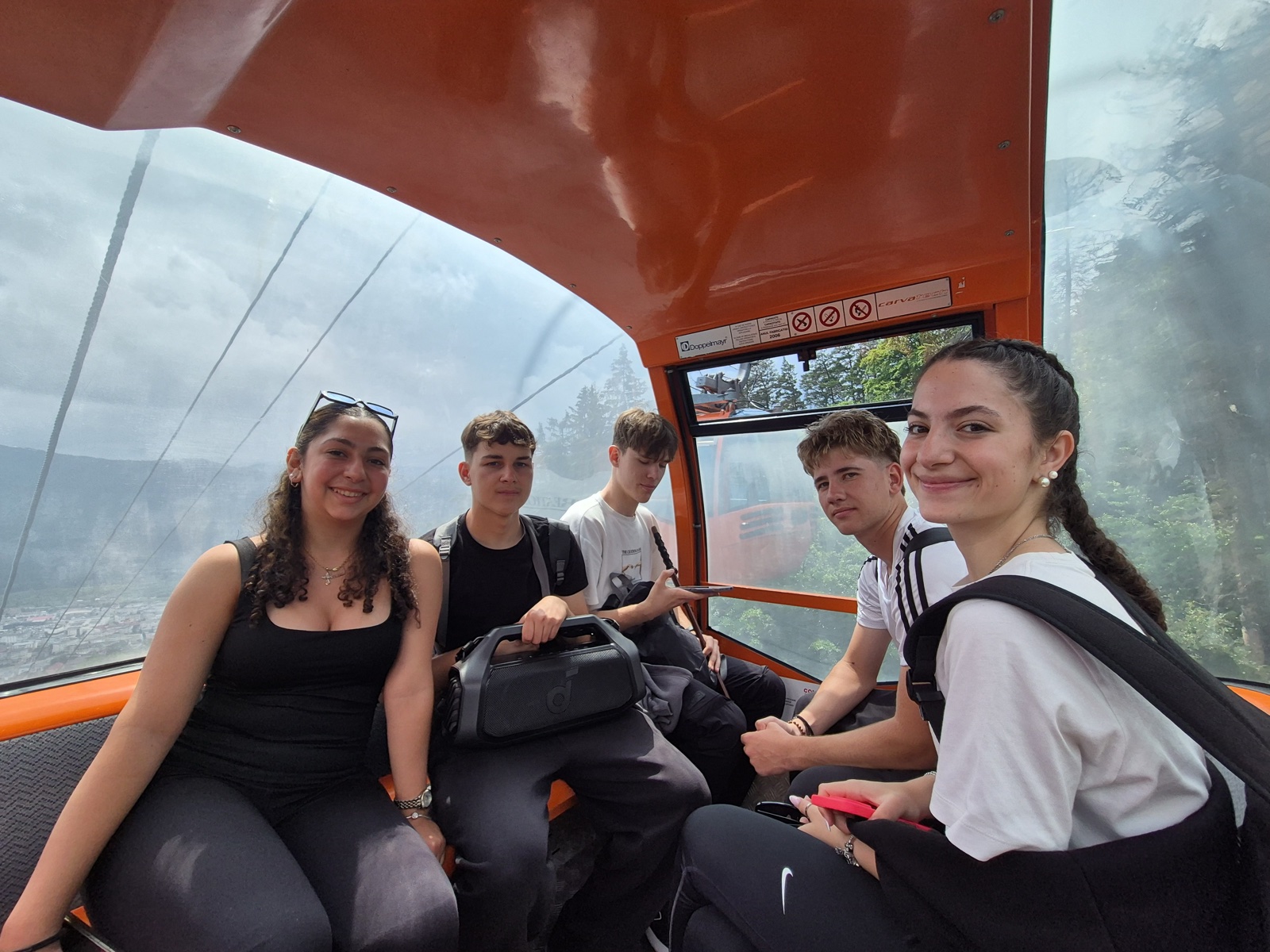 Five participants smile inside the orange cable-car cabin descending from Cozla