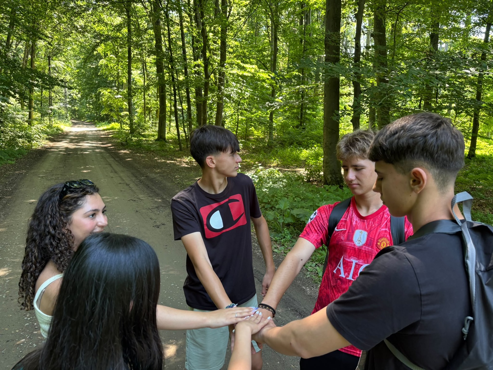 A team stacks hands in a circle on a forest road before the treasure hunt