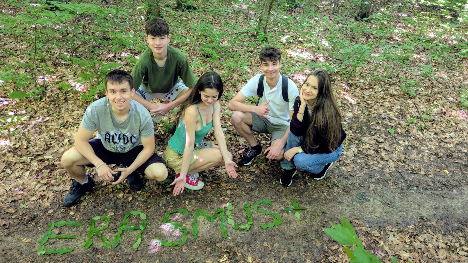 A treasure-hunt team crouches around ERASMUS+ written in leaves on the forest floor