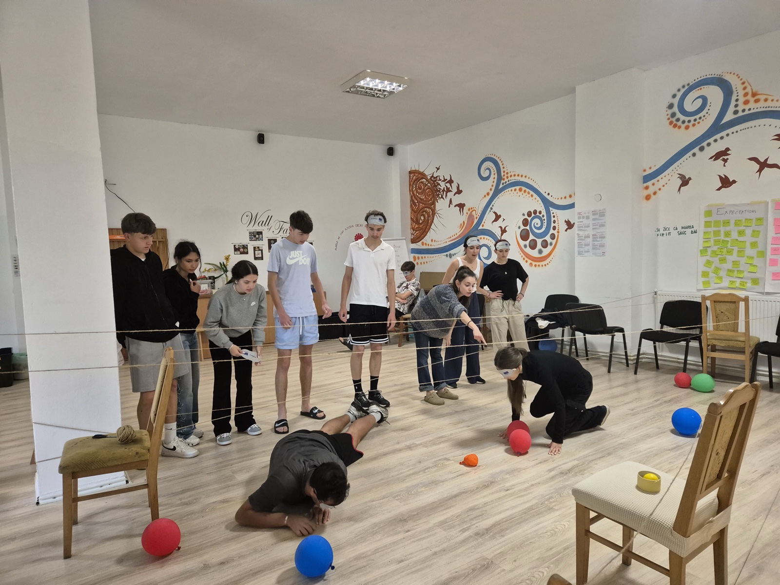 A participant crawls under a web of strings and balloons while the group watches