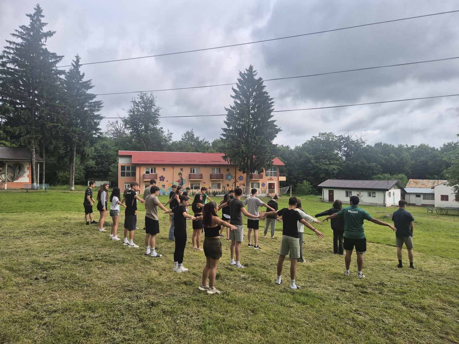 The group plays a childhood game with arms outstretched in a circle on the lawn