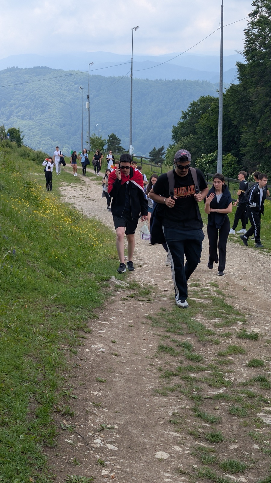 The group walks the summit path with mountains behind