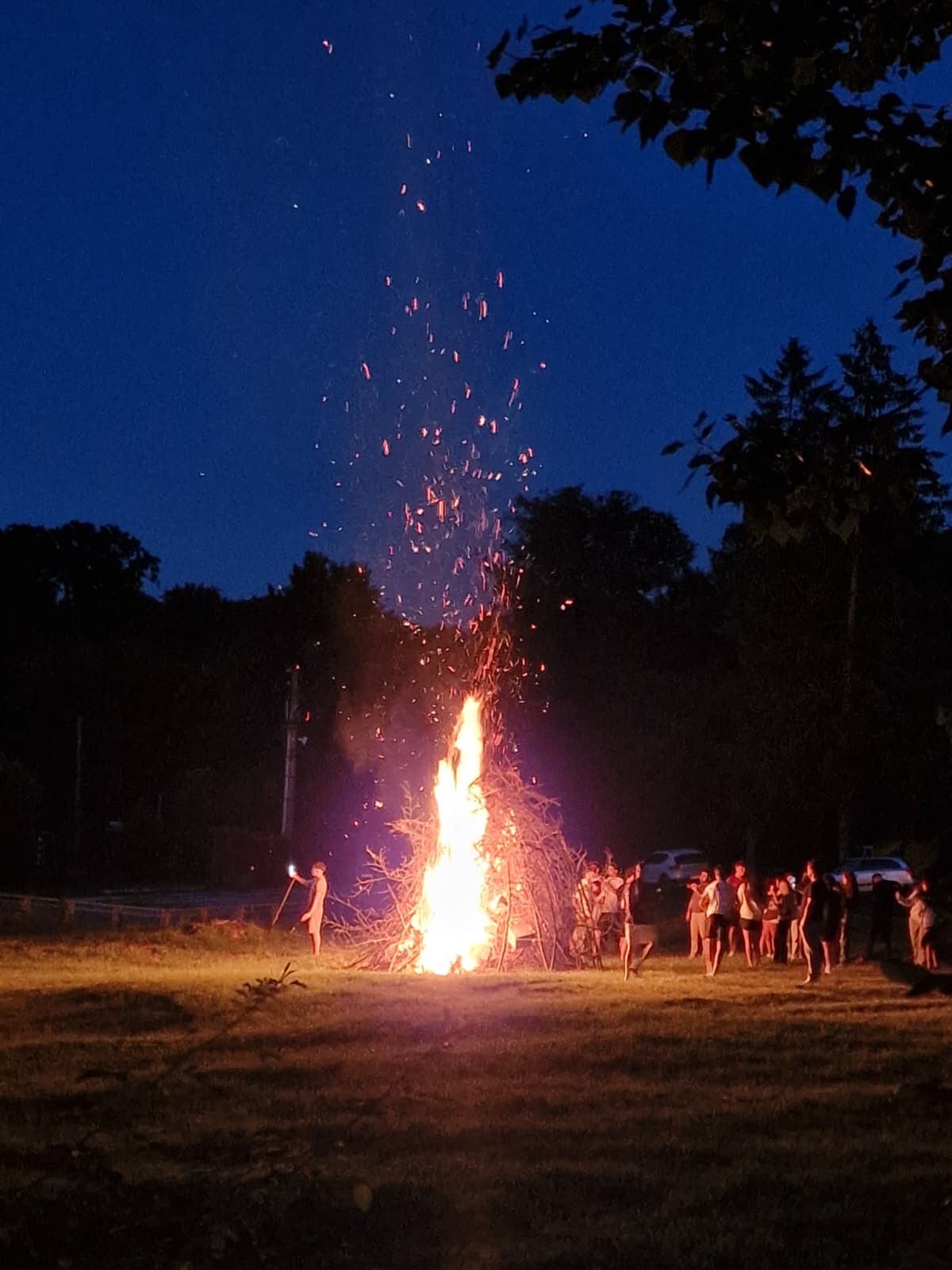 Sparks spiral up from the farewell bonfire at dusk