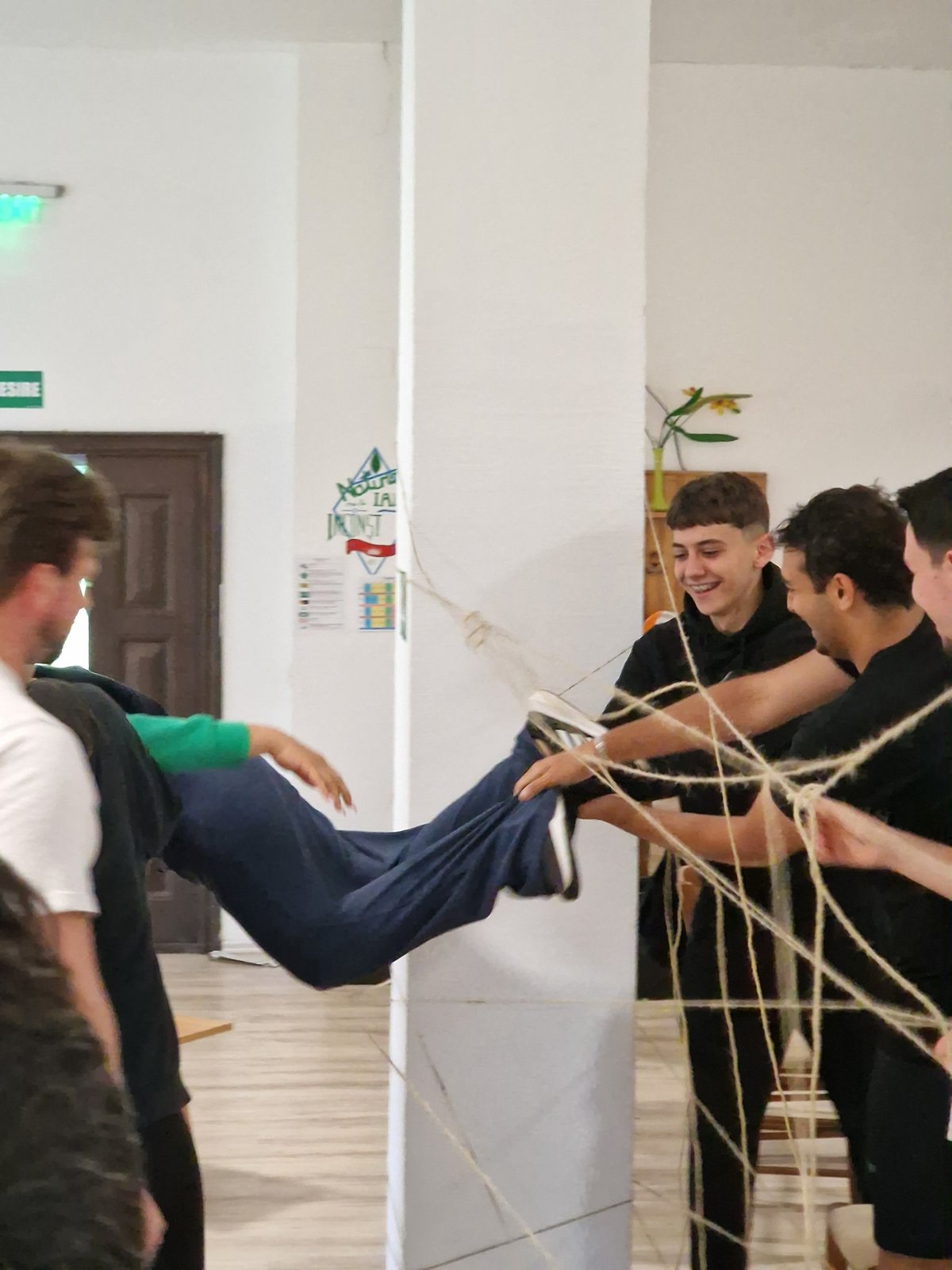 A participant is passed through the spider web of strings, hands everywhere to keep him off the threads